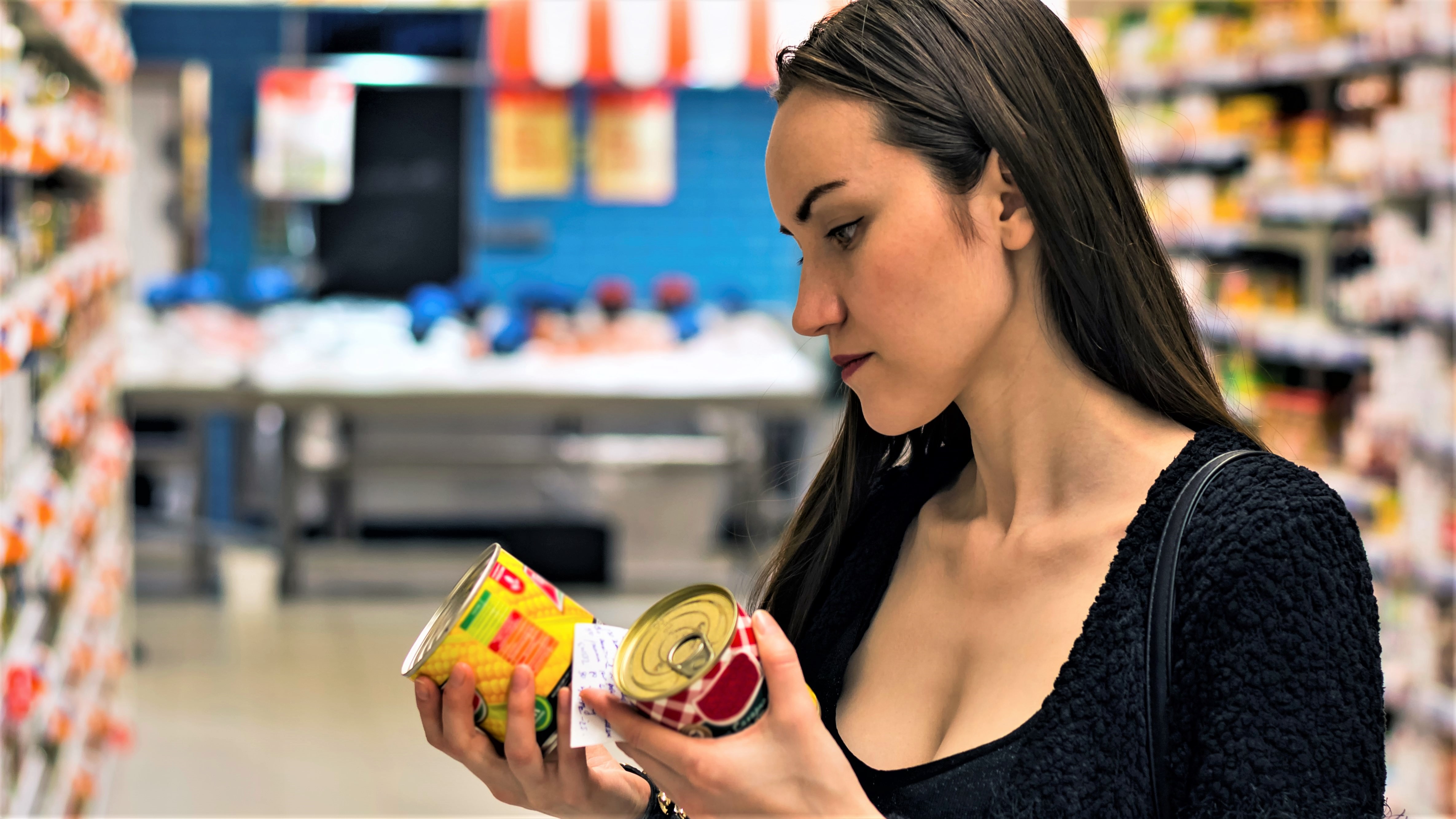 En kvinde står med to dåser i hånden i et supermarked og ser på etiketten