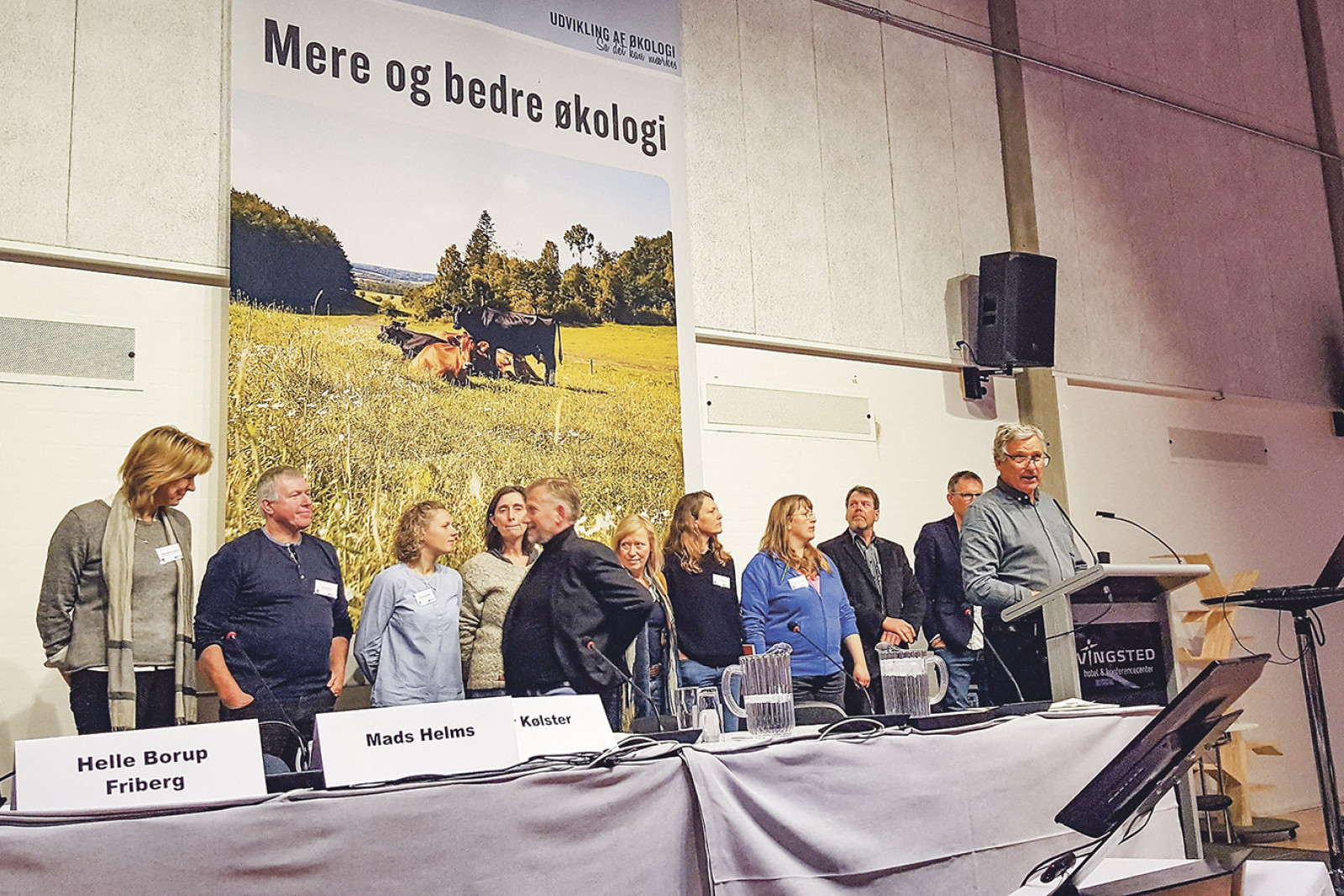 Bestyrelsesmedlemmer samt ØL's adm. direktør står side om side, mens Per Kølster står på talerstolen ved generalforsamlingen i 2018