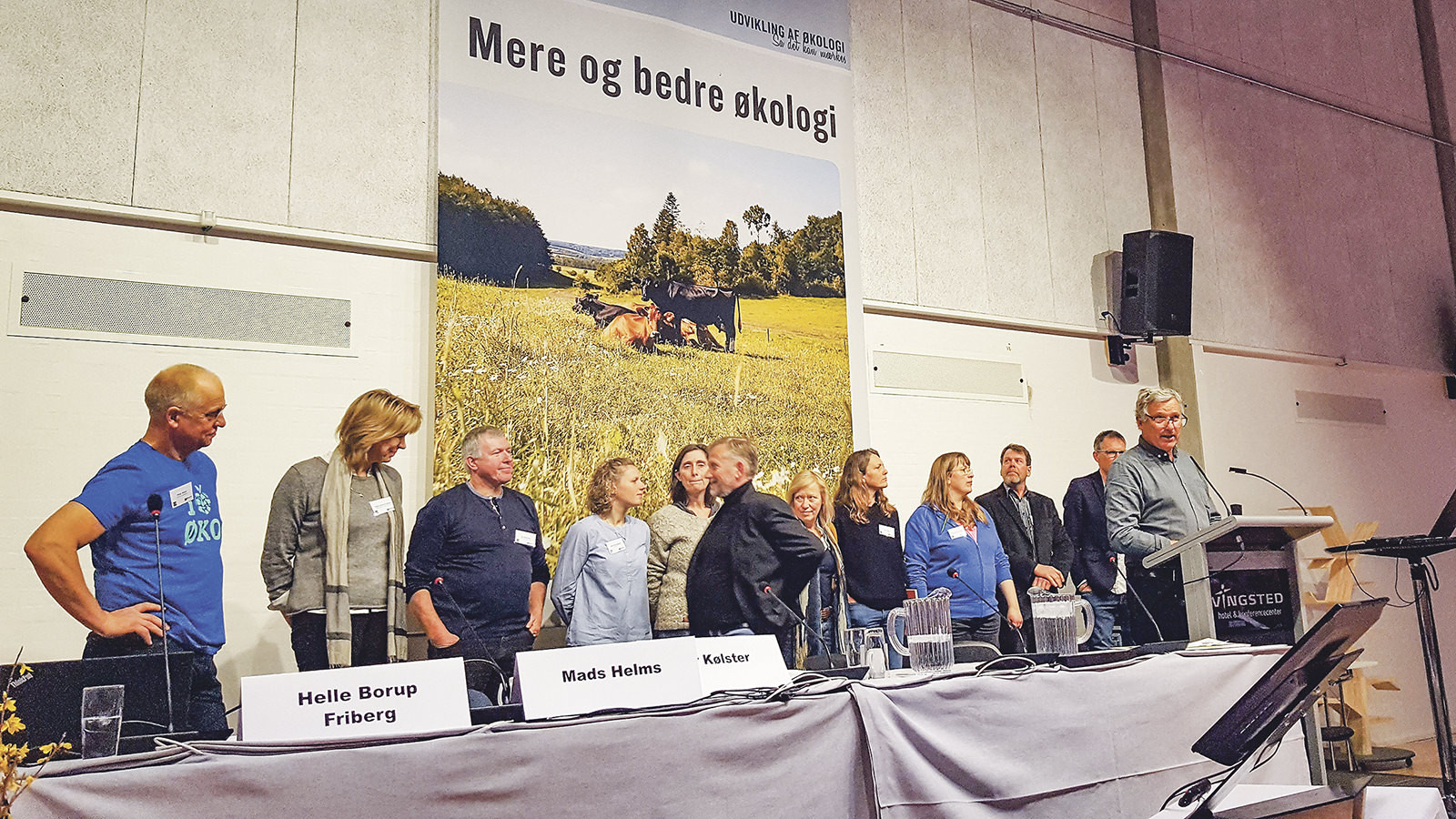 Bestyrelsesmedlemmer samt ØL's adm. direktør står side om side, mens Per Kølster står på talerstolen ved generalforsamlingen i 2018