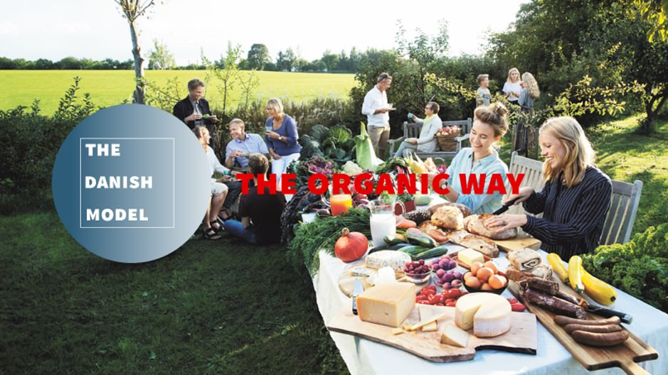 Omslag til magasinet 'The Organic Way - The Danish Model' med et havebord, der bugner med økologiske fødevarer