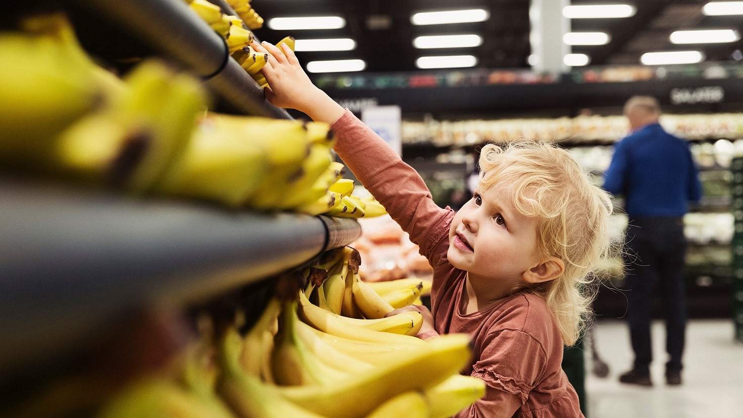 Lille pige rækker ud efter en øko-banan i dagligvarebutik.