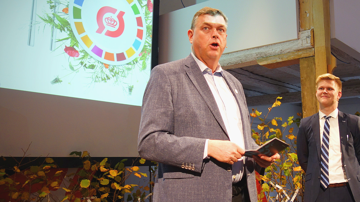 Fødevareminister Mogens Jensen taler fra scenen med Frederik Roland Sandby i baggrunden til økologisk topmøde 2019