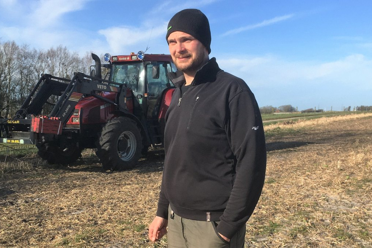 Søren Sandgaard på sin mark med en traktor i baggrunden