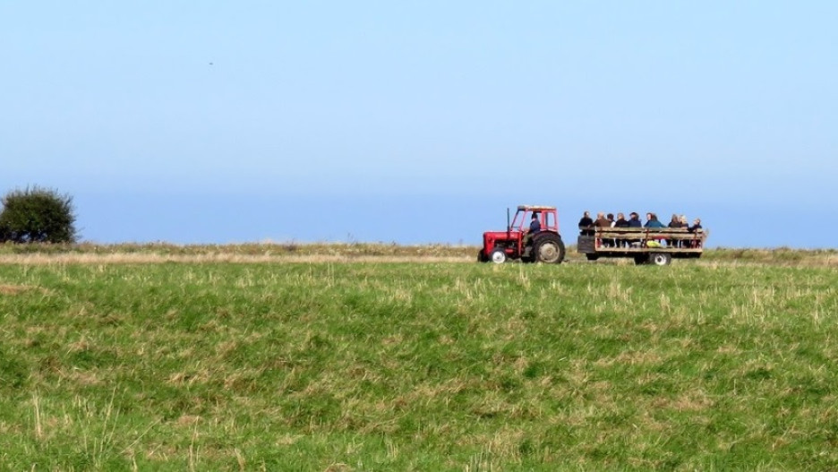 En traktor kører gennem landskabet med en påhængsvogn, hvorpå der sidder mennesker
